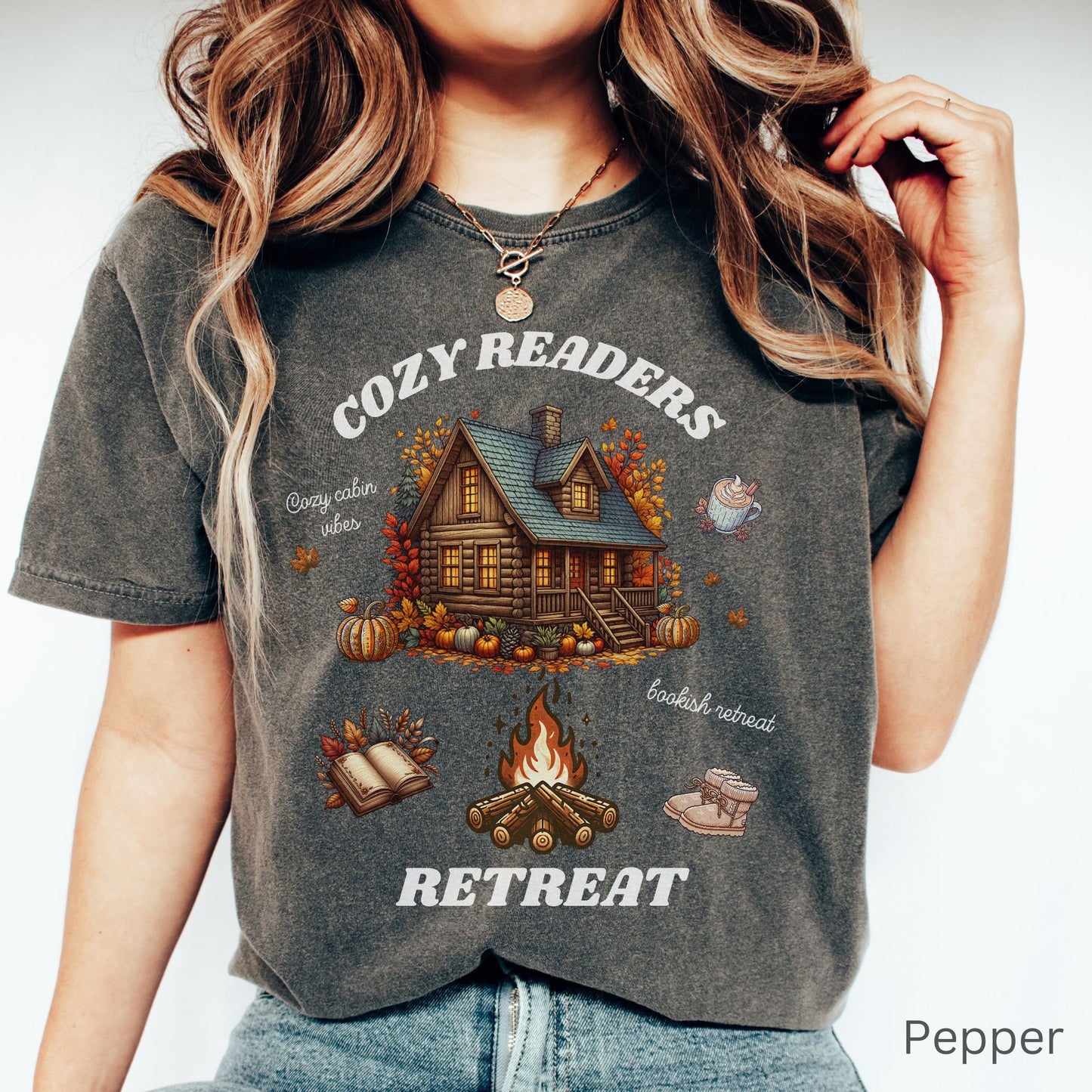 Woman wearing a Pepper Comfort Colors Tee with 'Cozy Readers Retreat' design including a cozy cabin, pumpkin spice latte, cute slippers, campfire, pumpkins and a book. Starlit Prose Bookish Merch Australia