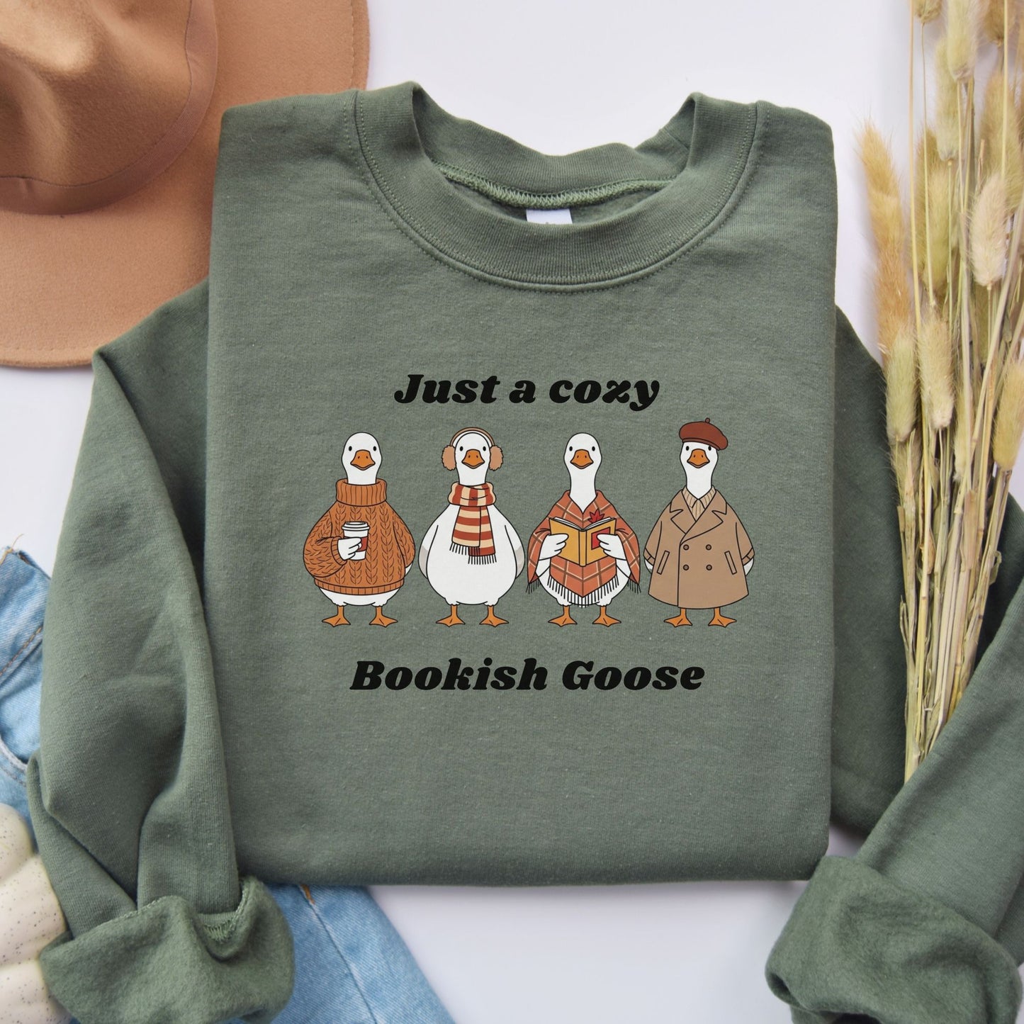 Green sweatshirt with cartoon geese and text that says "Just a Cozy Bookish Goose". Starlit Prose Bookish Merch Australia