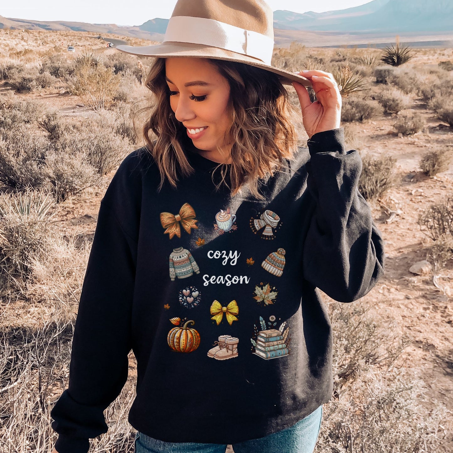 Woman wearing a Black sweatshirt with Fall-themed graphics and text, including a Pumpkin Spice Latte, scarf, beanie, stack of books, sweater & pumpkins sitting in a decorated room with pumpkins. Starlit Prose Bookish Merch Australia