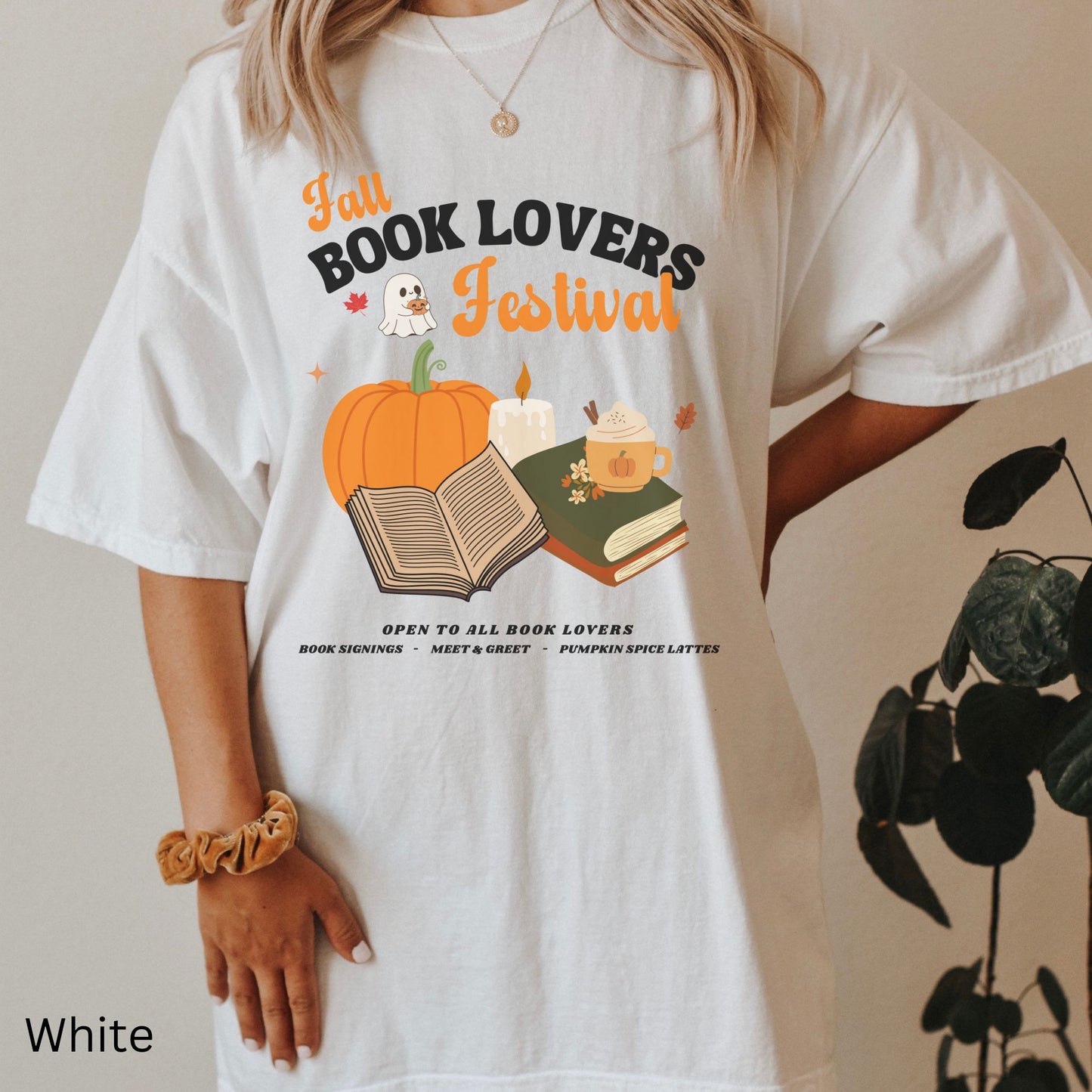 Woman wearing a White Comfort Colors Tshirt with 'Fall Book Lovers Festival' design featuring a pumpkin, books, and a ghost for a fictional Book Lovers Festival. Starlit Prose Bookish Merch Australia