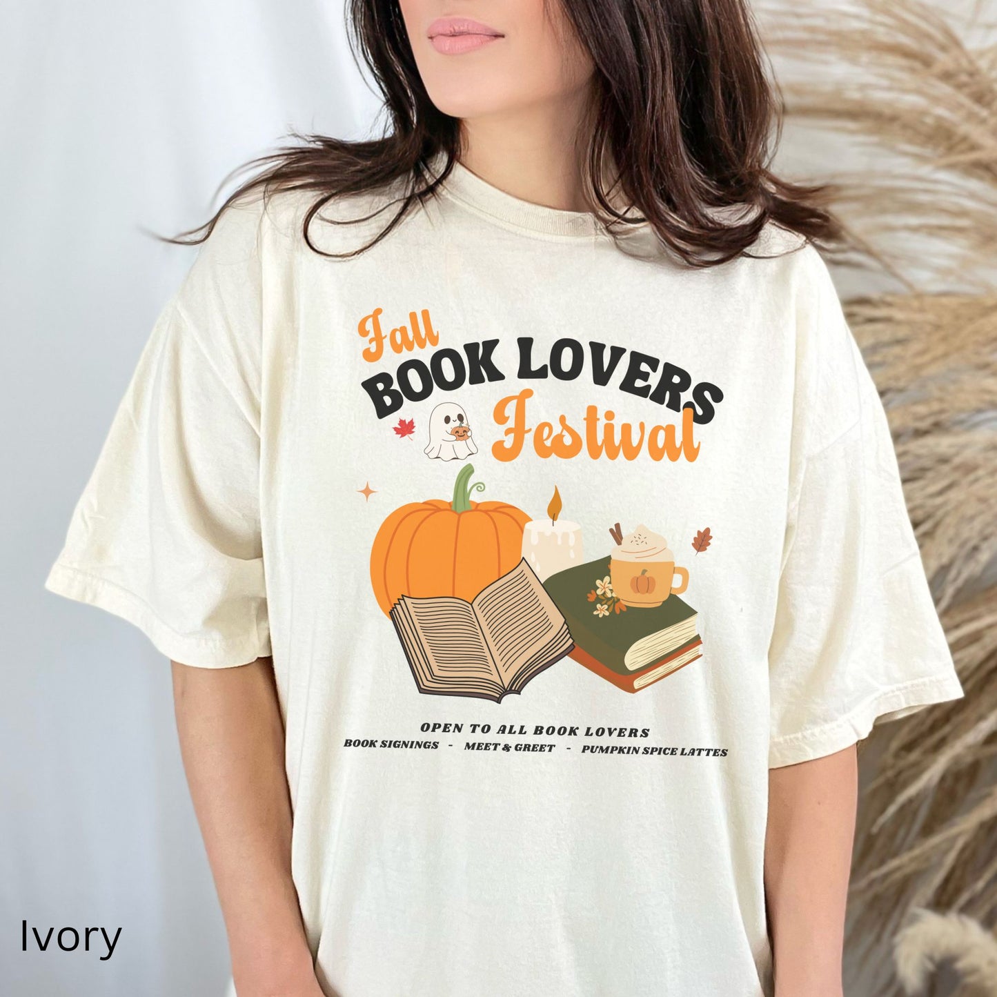 Woman wearing an Ivory Comfort Colors Tshirt with 'Fall Book Lovers Festival' design featuring a pumpkin, books, and a ghost for a fictional Book Lovers Festival. Starlit Prose Bookish Merch Australia
