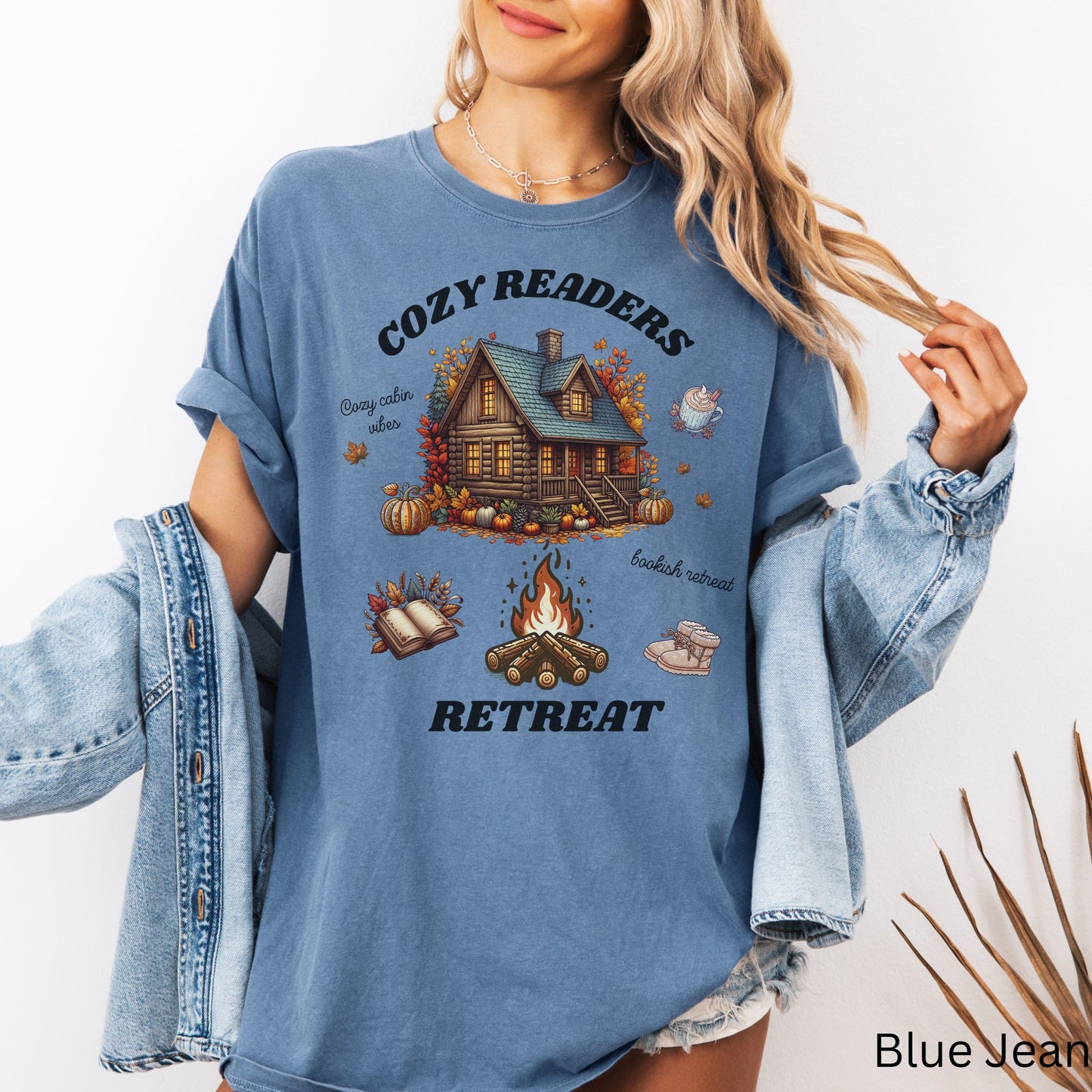 Woman wearing a Blue Jean Comfort Colors Tee with 'Cozy Readers Retreat' design including a cozy cabin, pumpkin spice latte, cute slippers, campfire, pumpkins and a book. Starlit Prose Bookish Merch Australia
