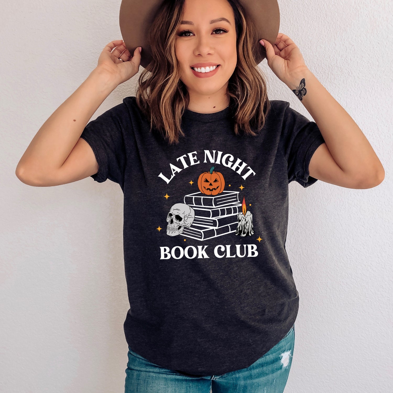 A woman wearing a tshirt that says "Late Night Book Club" with a graphic of a stack of books with a pumpkin and a skull.