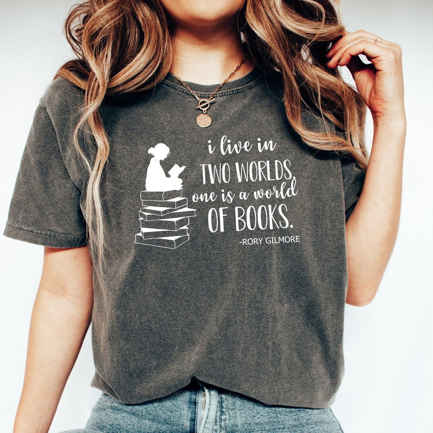 Starlit Prose Gilmore Girls collection - A woman is wearing a tshirt that says "I live in two worlds, one is a world of books" it has a graphic of a girl sitting on a stack of books reading.