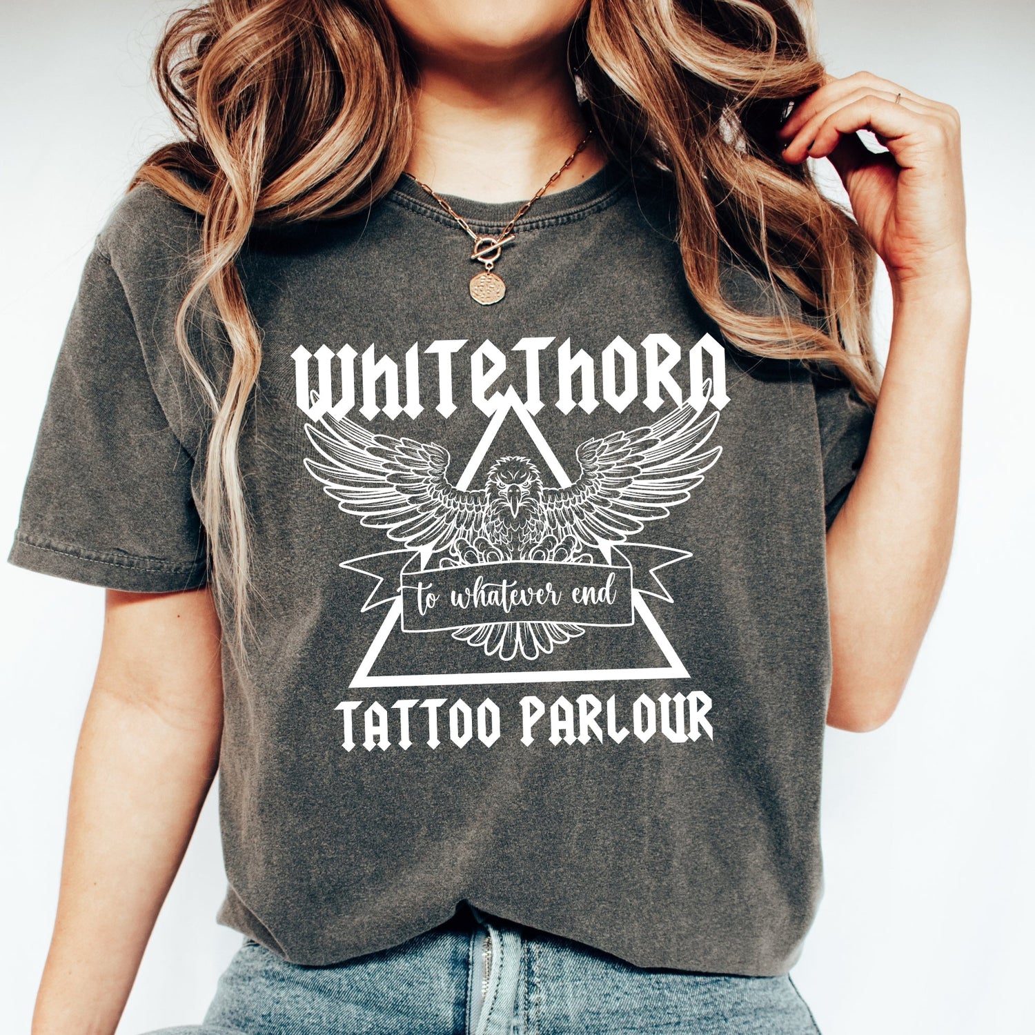 Woman wearing a Pepper Comfort colors shirt that has a design that says Whitethorn Tattoo Parlour and a graphic of a hawk. It also says to whatever end.