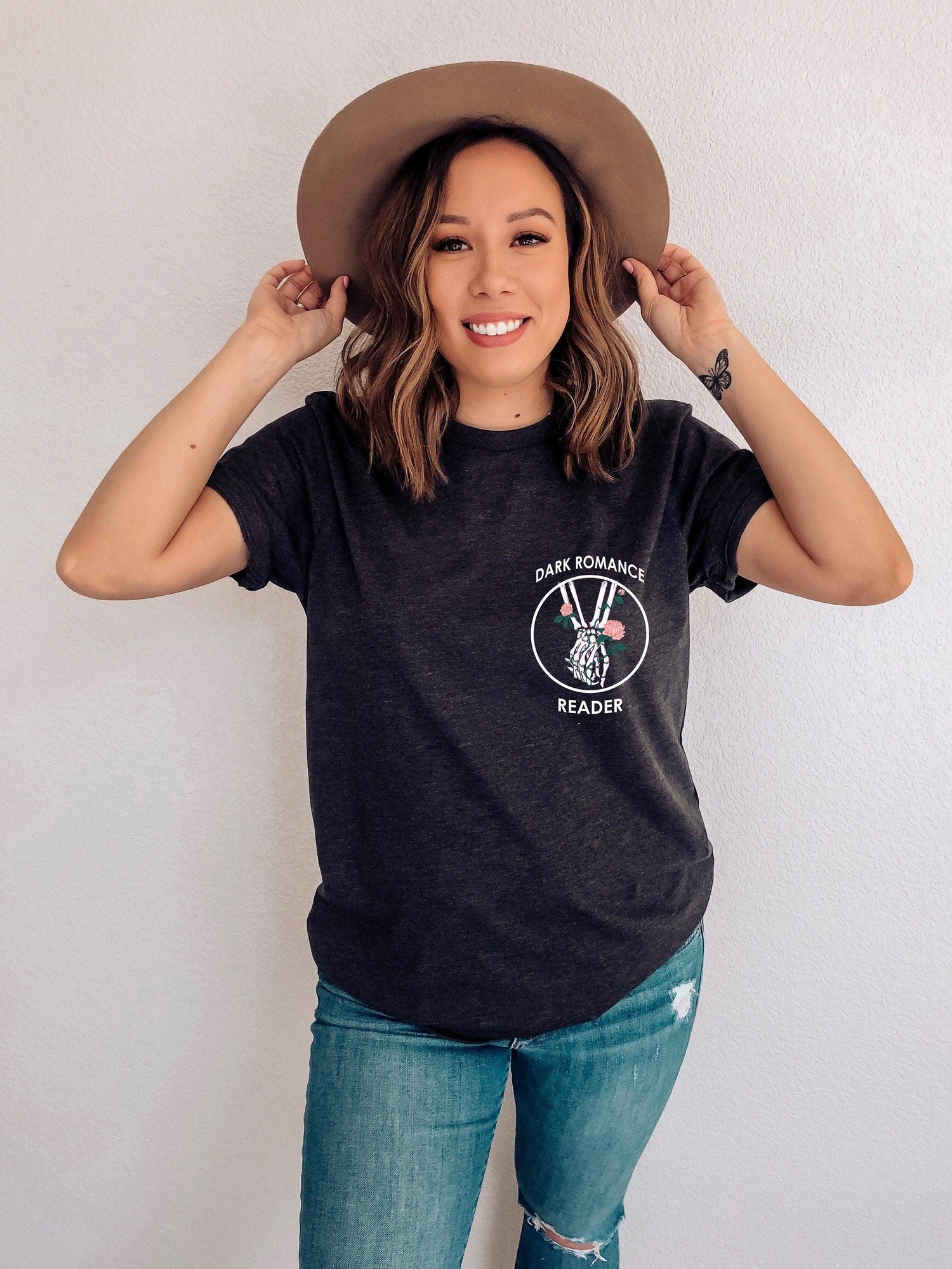 A woman wearing a dark grey heather tshirt with a design that says Dark Romance Reader with a graphic of two skeleton hands holding.