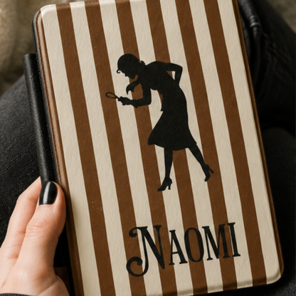 A close-up of a Personalised Nancy Drew Kindle Case, featuring a brown and cream vertical stripe pattern with a black silhouette of Nancy Drew holding a magnifying glass and a custom name in vintage style typography at the bottom. Designed by Starlit Prose Bookish Merch Australia.