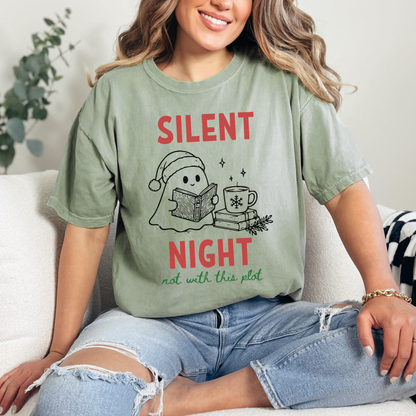 A woman wearing a Bay Green Comfort Colors t-shirt with a cute doodle illustration of a ghost reading a book, with a cup of coffee stacked on some books. There's bold text that says  'SILENT NIGHT" in red, with green cursive that says " not with this plot". Designed by Starlit Prose Bookish Merch Australia.