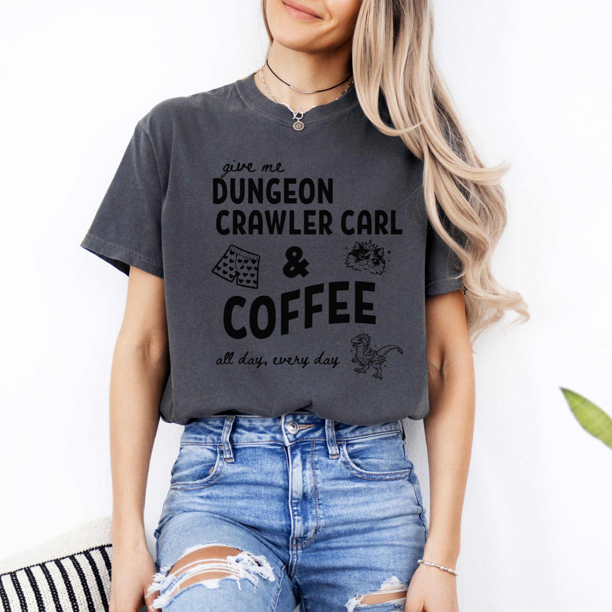 A woman wearing an oversized Pepper graphic Comfort colors T-shirt with black text reading 'give me DUNGEON CRAWLER CARL & COFFEE all day, every day' and small illustrations - including Carl's pajama shorts, Princess Donut & Mongo. Designed by Starlit Prose, Bookish Merch Australia