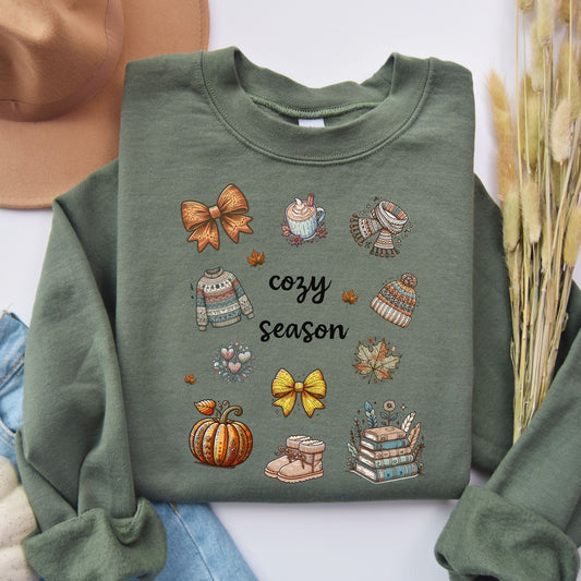 A Flatlay of a Green sweatshirt with Fall-themed graphics and text, including a Pumpkin Spice Latte, scarf, beanie, stack of books, sweater & pumpkins sitting in a decorated room with pumpkins. Starlit Prose Bookish Merch Australia