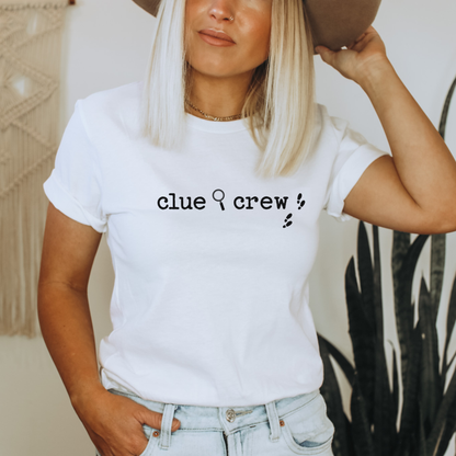 Person wearing a white t-shirt with 'clue crew' text, holding a hat.