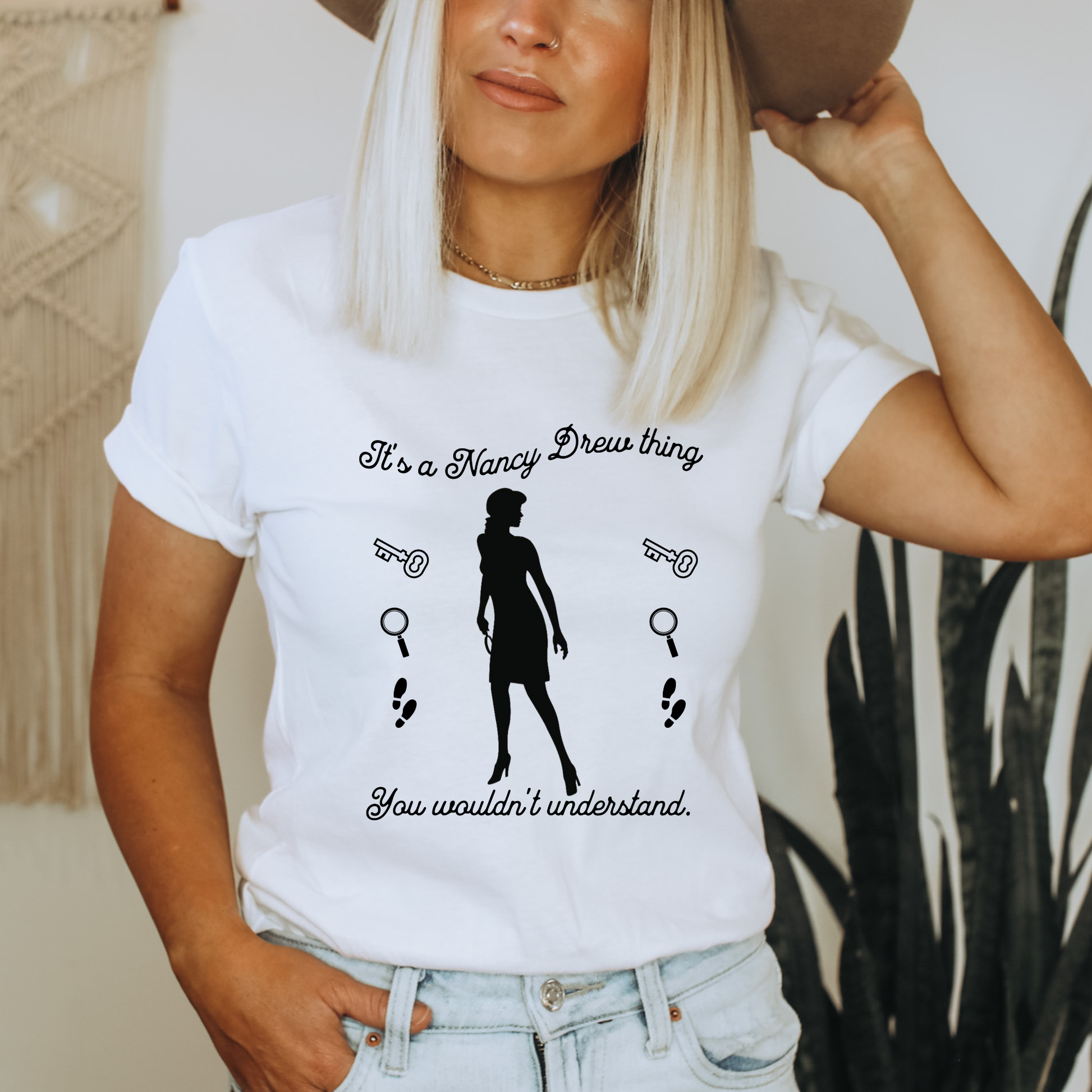 white tshirt with text that says "It's a Nancy Drew thing, you wouldn't understand" with graphic elements like a key, magnifying glass and footsteps.