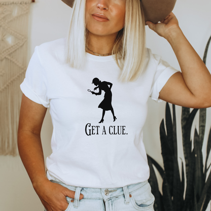 Person wearing a white t-shirt with a black silhouette and 'GET A CLUE.' text, holding a brown hat.
