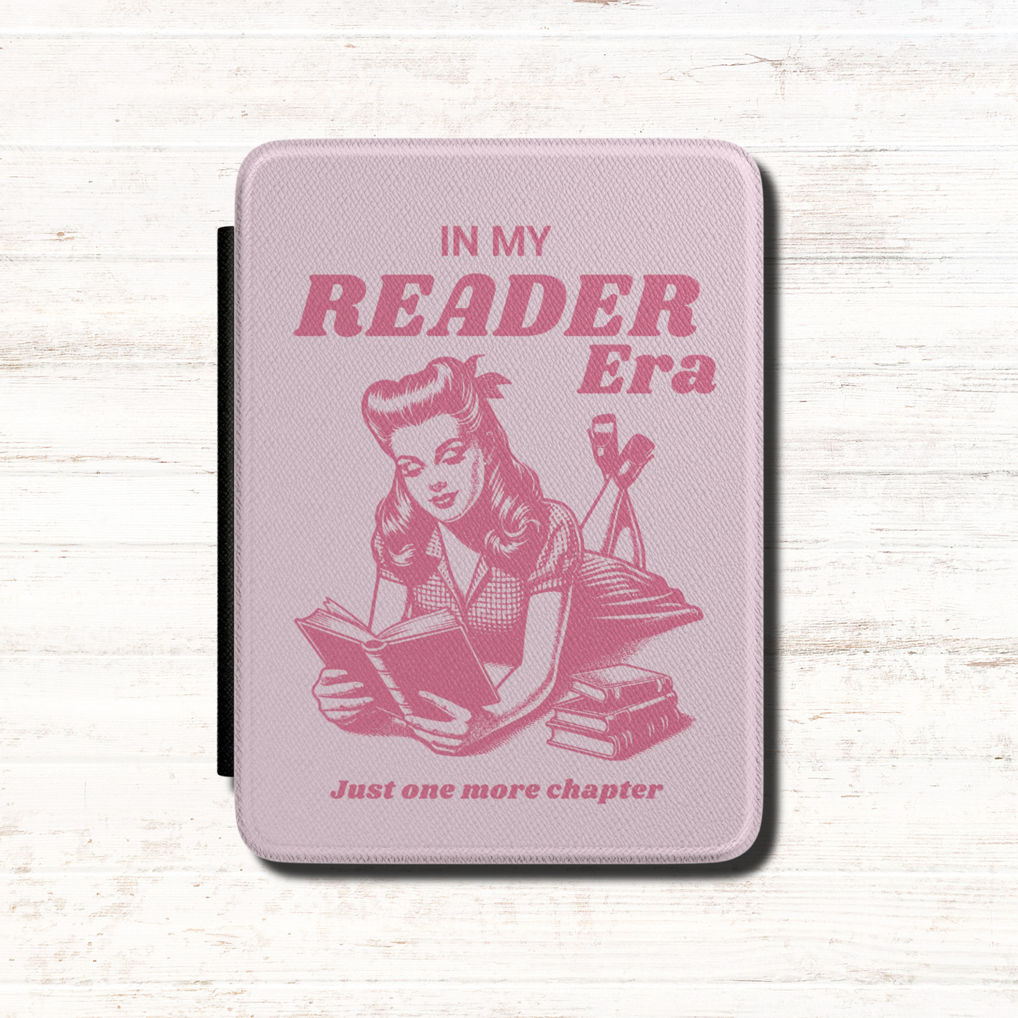 This playful pink Bookish In my Reader Era Kindle case features a vintage pin-up-inspired reader lounging with her book, paired with the phrases "In My Reader Era" and "Just One More Chapter." Pink background. Designed by Starlit Prose Bookish Merch Australia.