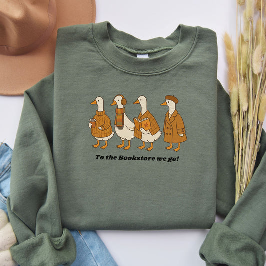 Green sweatshirt with cartoon ducks in coats and a hat, text 'To the Bookstore we go!', on a white background. Starlit Prose Bookish Merch Australia