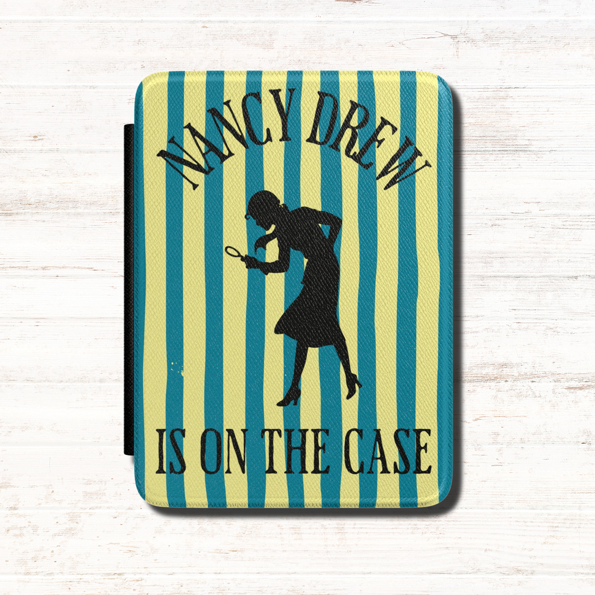 A Nancy Drew Kindle Case that features yellow and blue stripes, with a black silhouette of Nancy Drew with a magnifying glass and the text 'NANCY DREW IS ON THE CASE'. Designed by Starlit Prose Bookish Merch Australia.