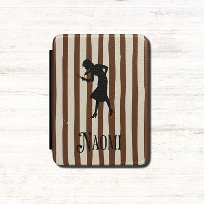 A close-up of a Personalised Nancy Drew Kindle Case, featuring a brown and cream vertical stripe pattern with a black silhouette of Nancy Drew holding a magnifying glass and a custom name in vintage style typography at the bottom. Designed by Starlit Prose Bookish Merch Australia.
