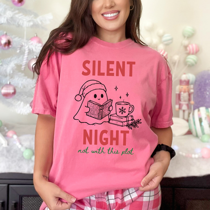 A woman wearing a Crunchberry Pink Comfort Colors t-shirt with a cute doodle illustration of a ghost reading a book, with a cup of coffee stacked on some books. There's bold text that says  'SILENT NIGHT" in red, with green cursive that says " not with this plot". Designed by Starlit Prose Bookish Merch Australia.