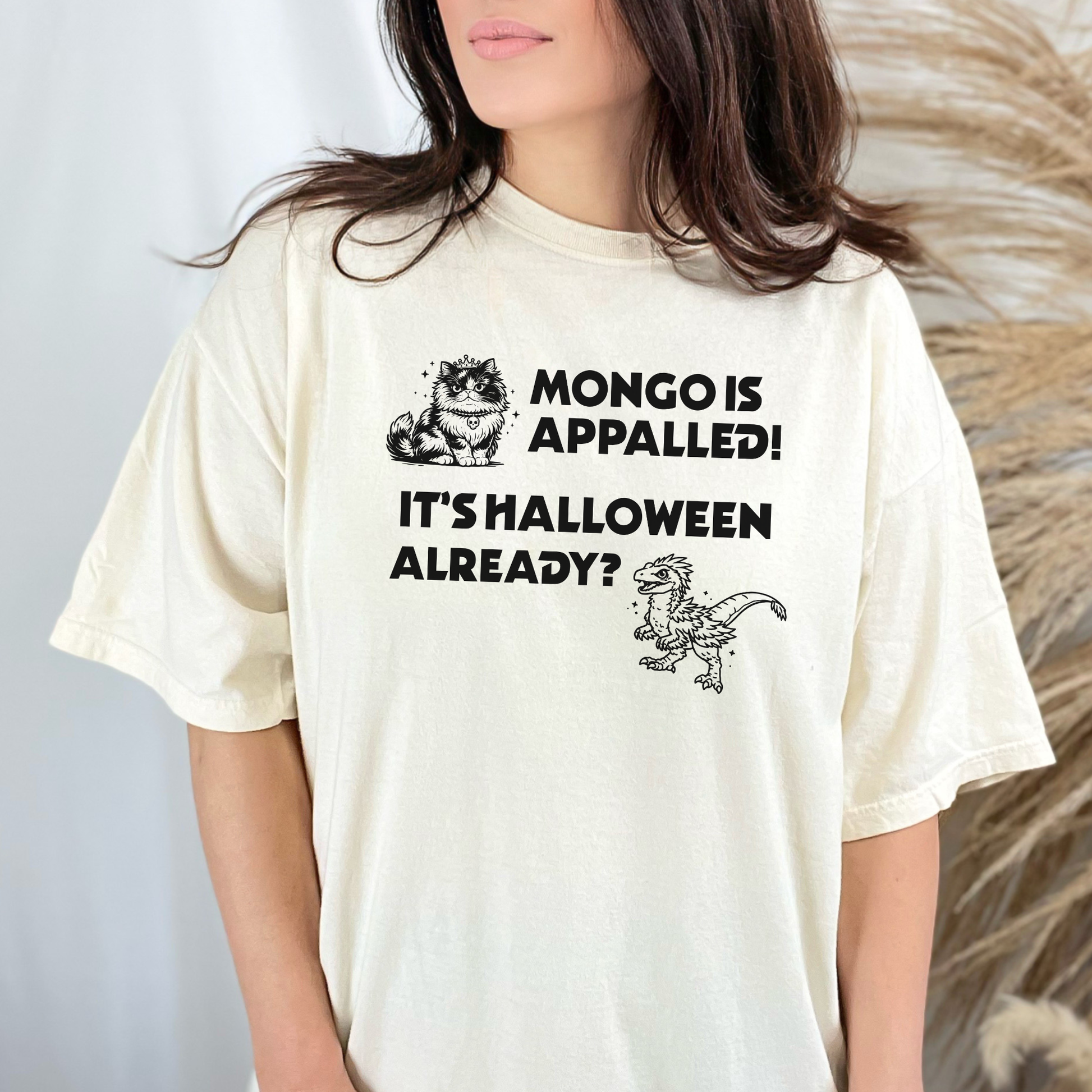 A woman wearing an Ivory Comfort Colors t-shirt with a Halloween design that reads 'MONGO IS APPALLED! IT'S HALLOWEEN ALREADY?' with illustrations of Princess Donut and Mongo. Designed by Starlit Prose Bookish Merch Australia