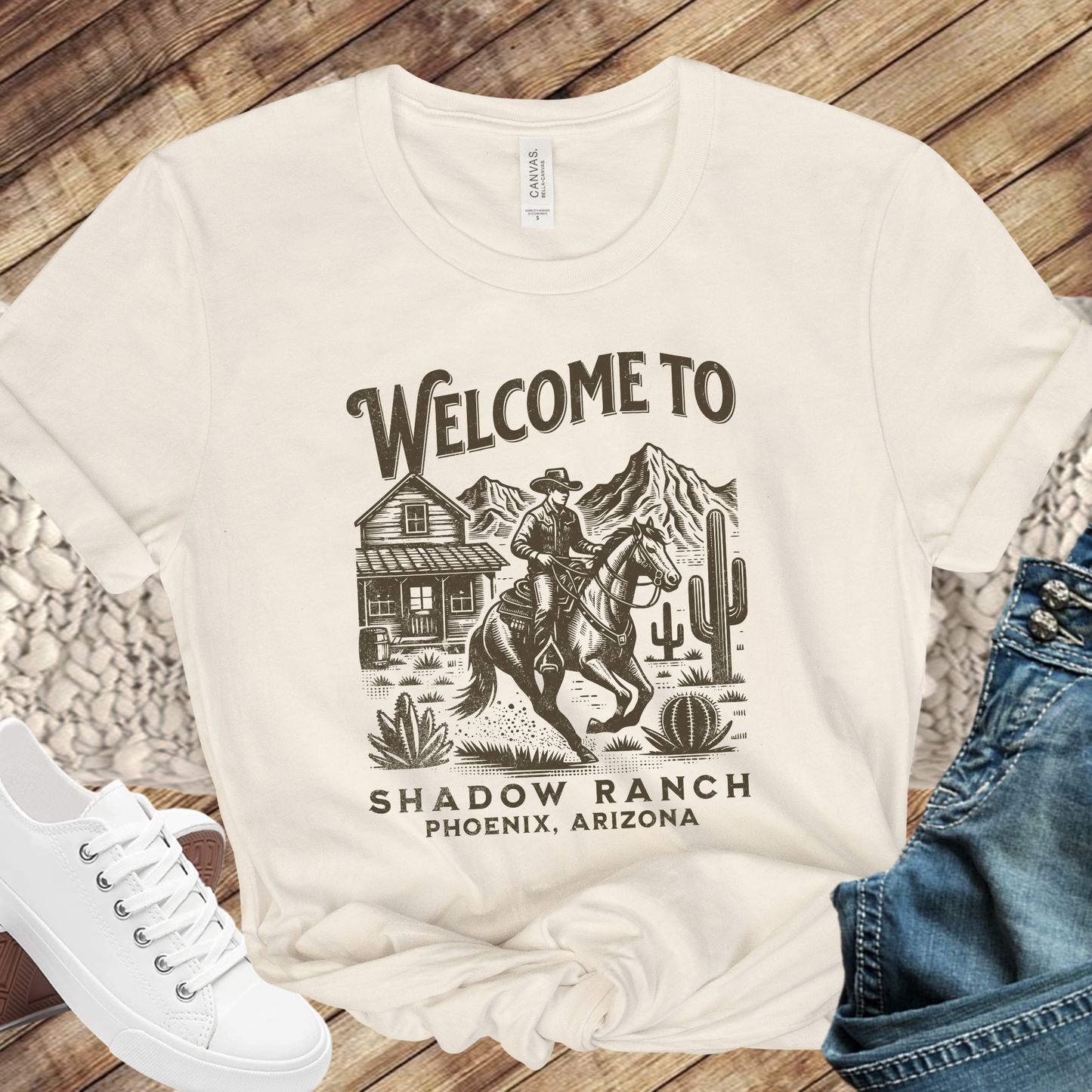 beige shirt that says "Welcome to Shadow Ranch Phoenix, Arizona" with a retro graphic of a cowboy riding on a horse.