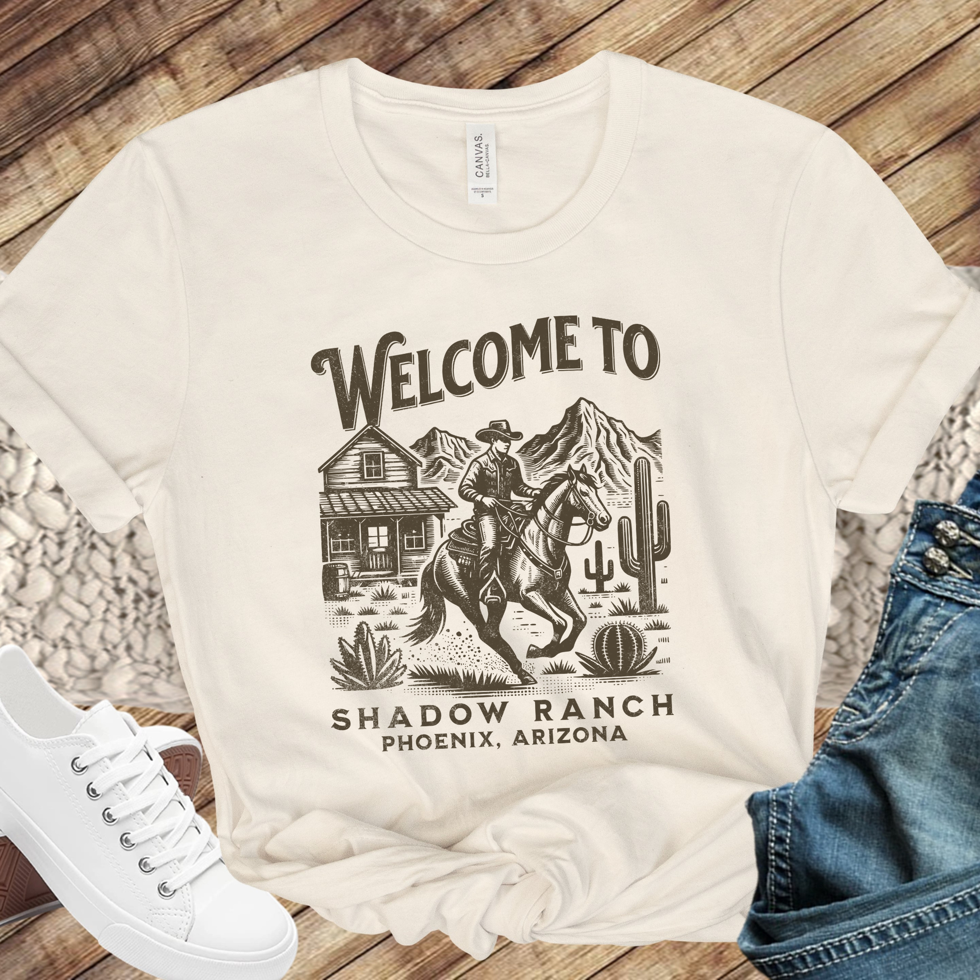 beige shirt that says "Welcome to Shadow Ranch Phoenix, Arizona" with a retro graphic of a cowboy riding on a horse.