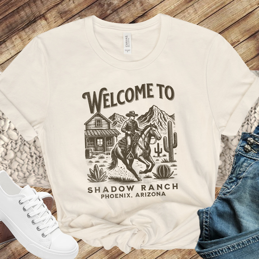 beige shirt that says "Welcome to Shadow Ranch Phoenix, Arizona" with a retro graphic of a cowboy riding on a horse.