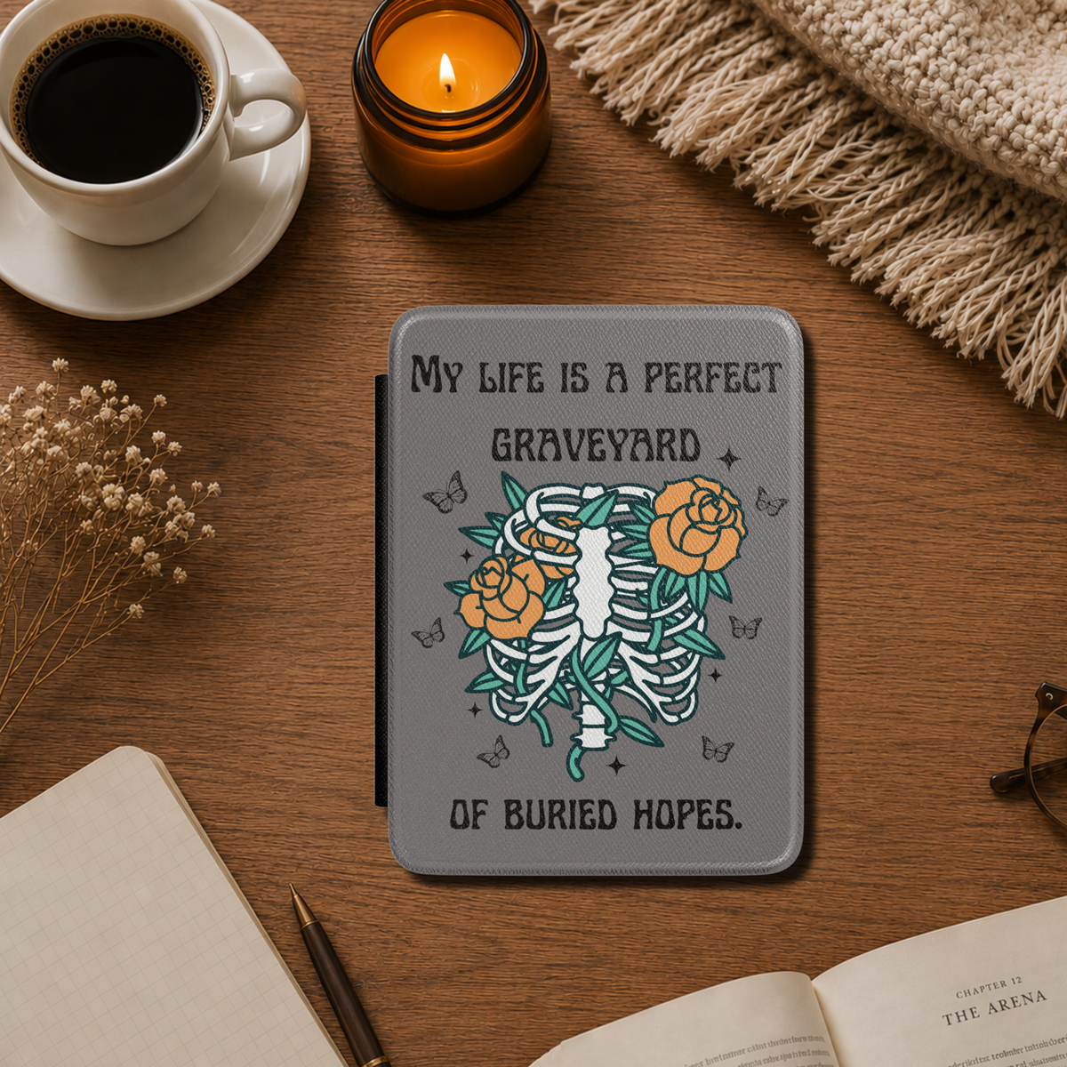 This dark literary Kindle case features the haunting quote "My life is a perfect graveyard of buried hopes" from Anne of Green Gables, paired with an illustrated skeletal ribcage from which delicate flowers and twisting vines emerge. It has a dark grey background. Designed by Starlit Prose Bookish Merch Australia.