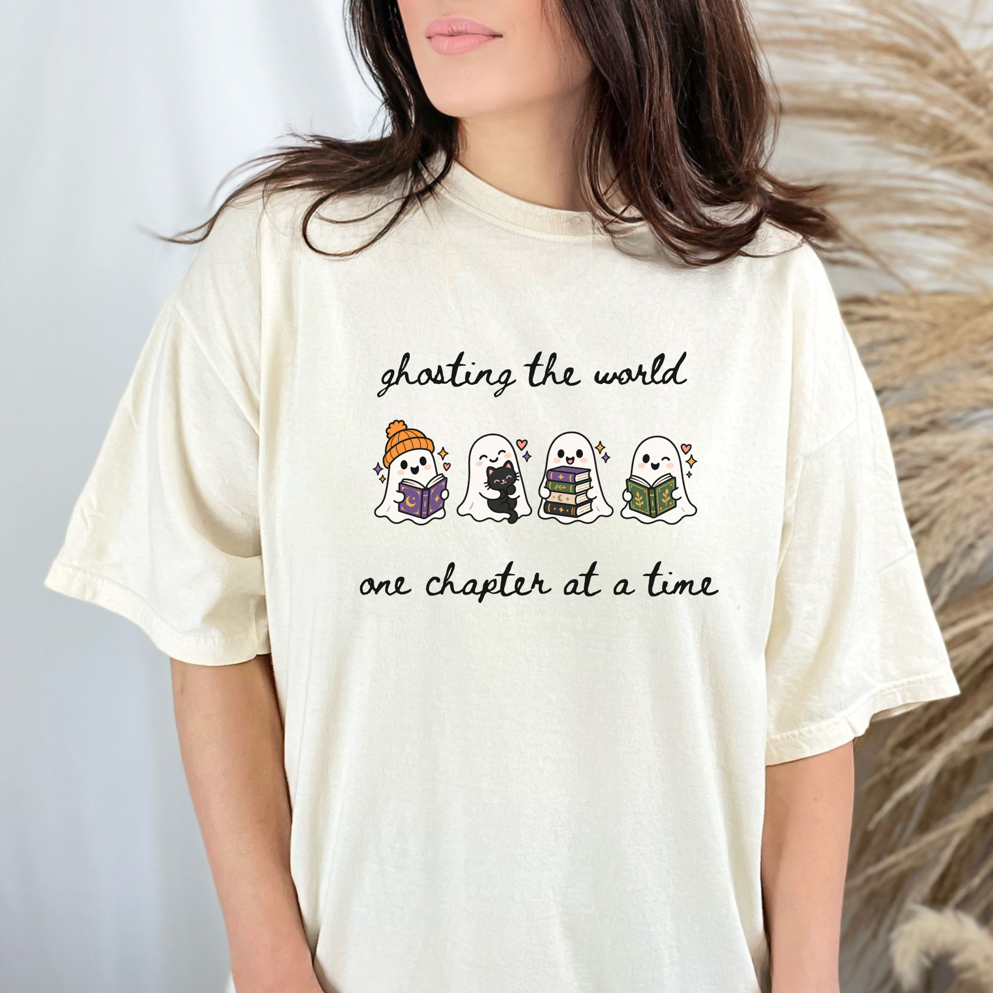 A woman wearing an oversized Ivory Comfort Colors T-shirt with four cartoon ghosts reading books and the text 'ghosting the world one chapter at a time". Designed by Starlit Prose Bookish Merch Australia