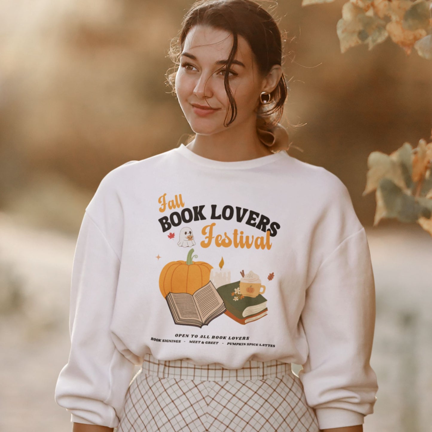 Woman wearing a white sweatshirt with 'Fall Book Lovers Festival' design featuring a pumpkin, books, and a ghost for a fictional Book Lovers Festival. Starlit Prose Bookish Merch Australia