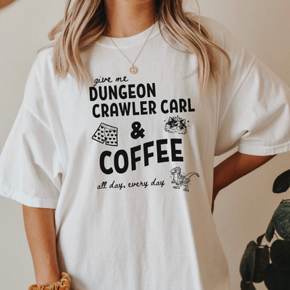 A woman wearing an oversized white graphic Comfort colors T-shirt with black text reading 'give me DUNGEON CRAWLER CARL & COFFEE all day, every day' and small illustrations - including Carl's pajama shorts, Princess Donut & Mongo. Designed by Starlit Prose, Bookish Merch Australia
