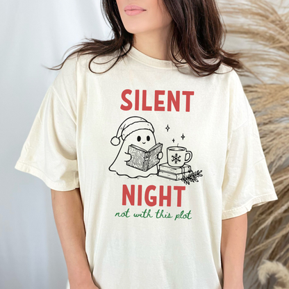 A woman wearing an Ivory Comfort Colors t-shirt with a cute doodle illustration of a ghost reading a book, with a cup of coffee stacked on some books. There's bold text that says  'SILENT NIGHT" in red, with green cursive that says " not with this plot". Designed by Starlit Prose Bookish Merch Australia.