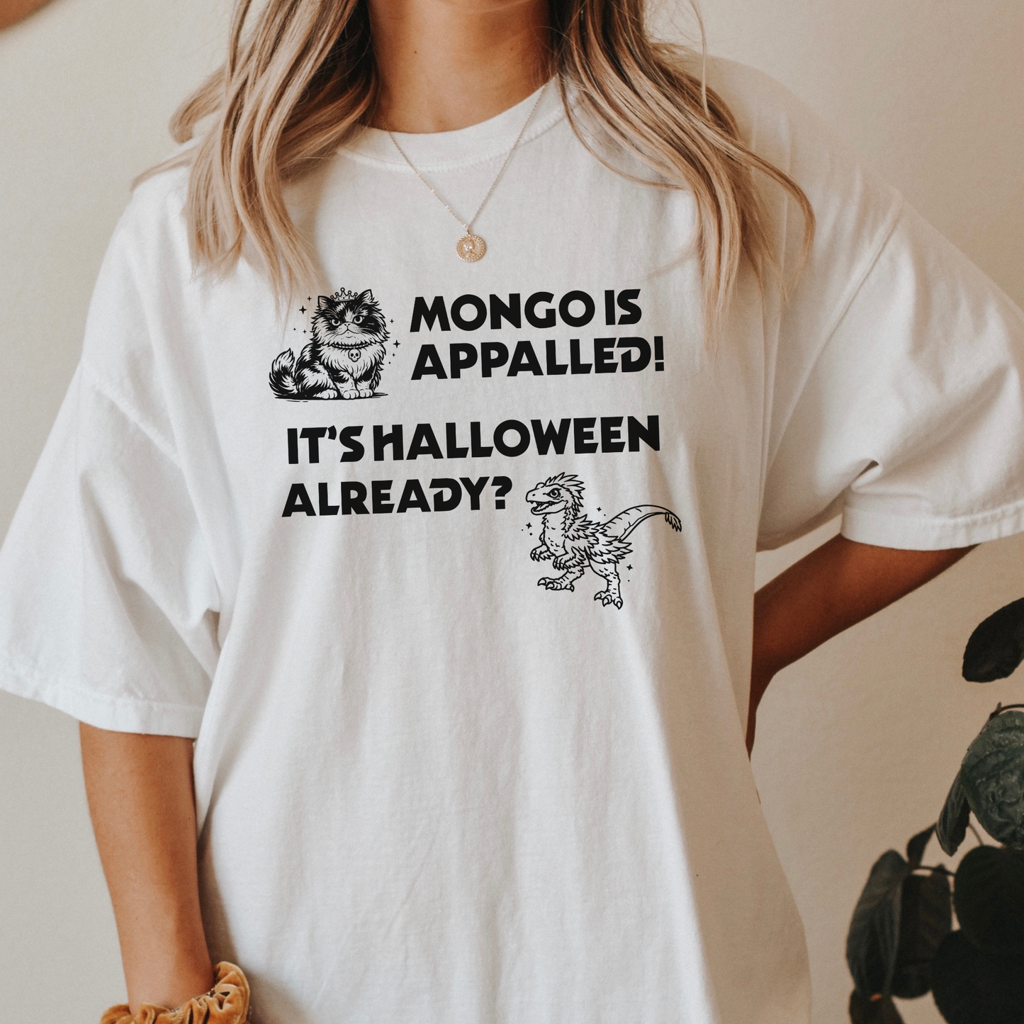 A woman wearing a White Comfort Colors t-shirt with a Halloween design that reads 'MONGO IS APPALLED! IT'S HALLOWEEN ALREADY?' with illustrations of Princess Donut and Mongo. Designed by Starlit Prose Bookish Merch Australia