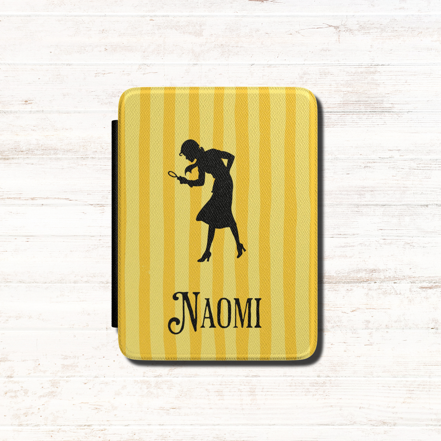A close-up of a Personalised Nancy Drew Kindle Case, featuring a yellow vertical stripe pattern with a black silhouette of Nancy Drew holding a magnifying glass and a custom name in vintage style typography at the bottom. Designed by Starlit Prose Bookish Merch Australia.