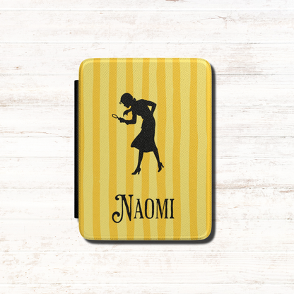 A close-up of a Personalised Nancy Drew Kindle Case, featuring a yellow vertical stripe pattern with a black silhouette of Nancy Drew holding a magnifying glass and a custom name in vintage style typography at the bottom. Designed by Starlit Prose Bookish Merch Australia.