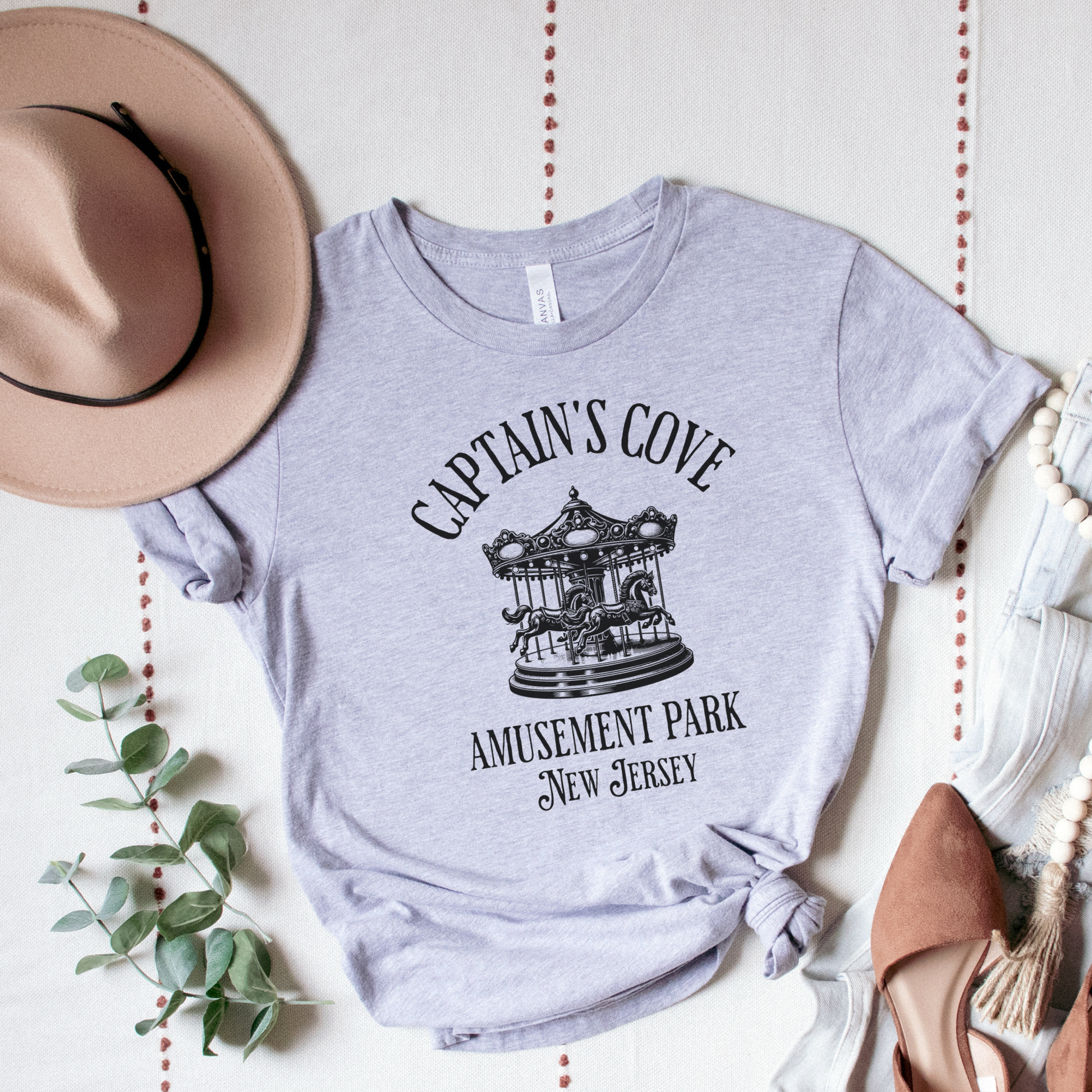 Gray t-shirt with 'Captain's Cove Amusement Park New Jersey' design on a white surface with decorative elements.