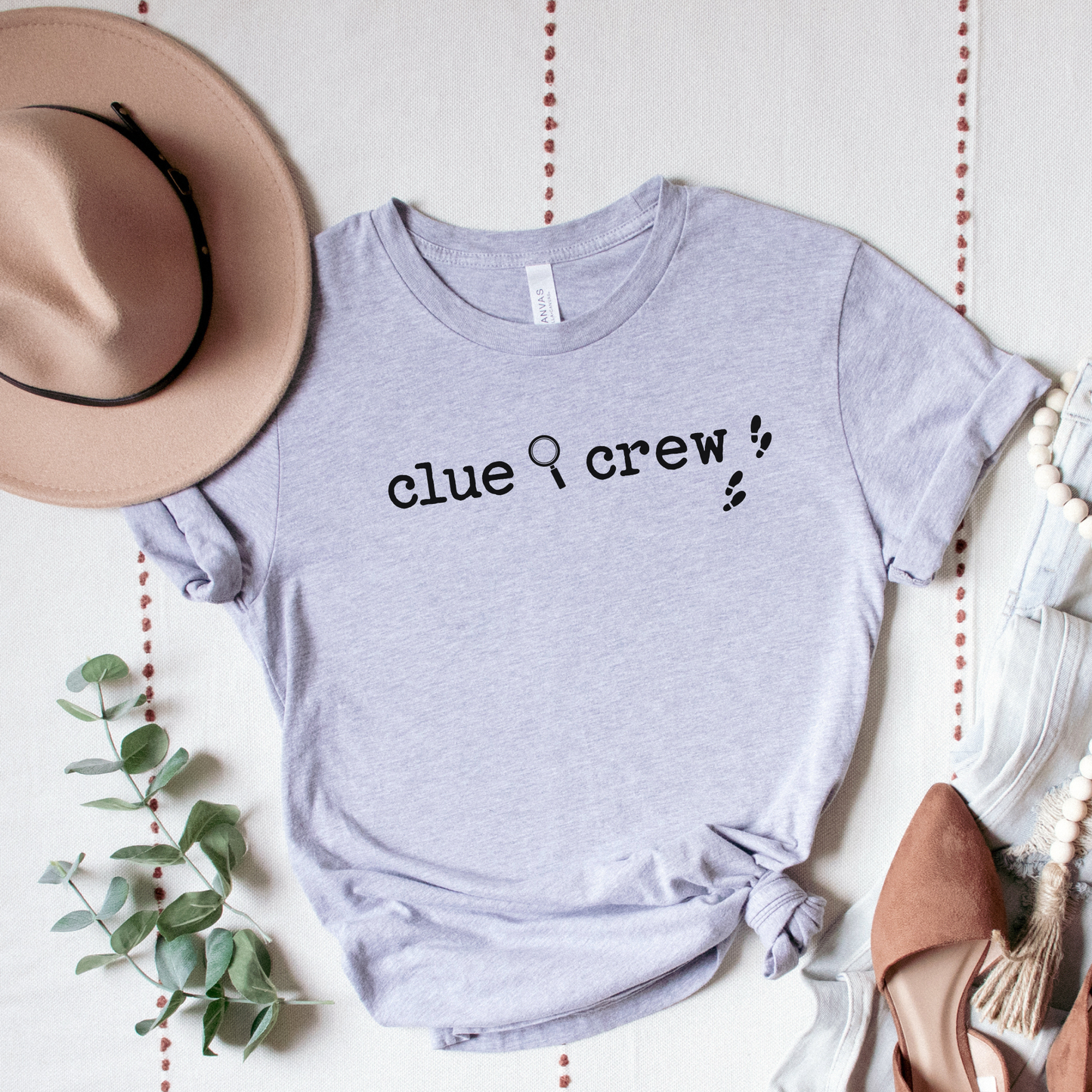 Gray t-shirt with 'clue crew' text, surrounded by a hat, shoes, and decorative elements on a light background