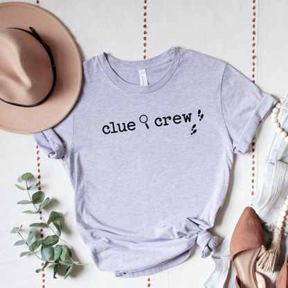 Gray t-shirt with 'clue crew' text, surrounded by a hat, shoes, and decorative elements on a light background