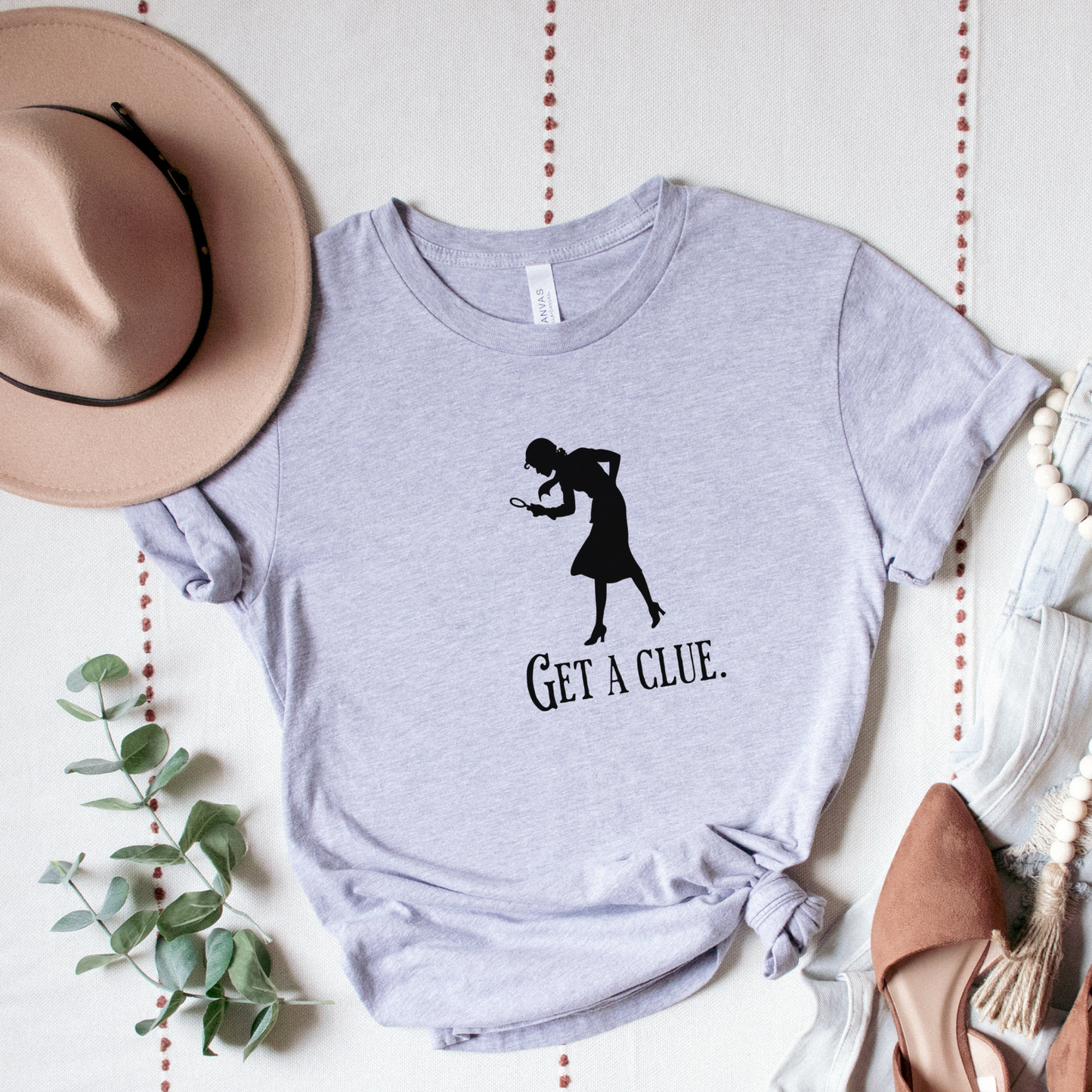 Gray t-shirt with a graphic and text 'GET A CLUE.' on a light background with decorative elements.