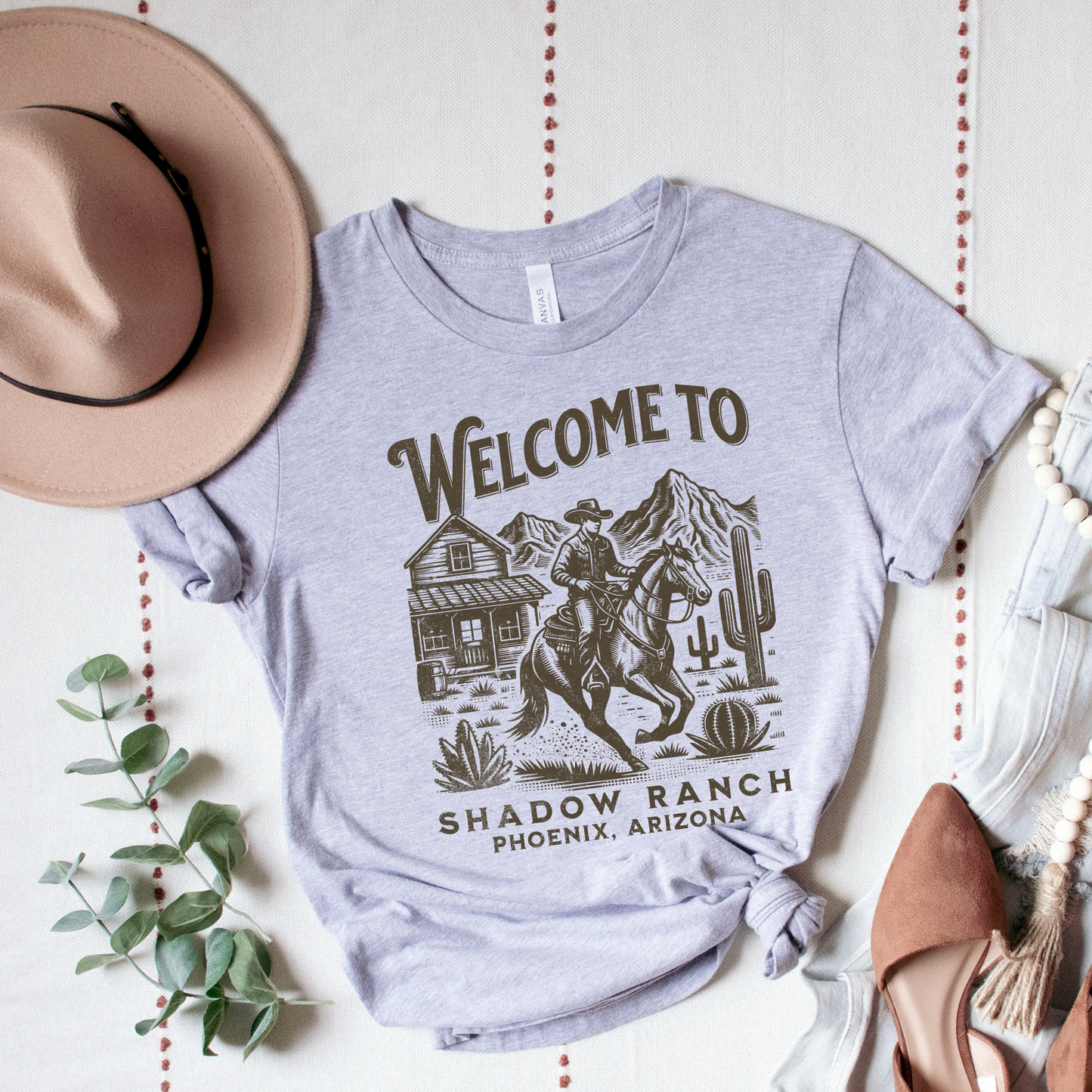 grey shirt that says "Welcome to Shadow Ranch Phoenix, Arizona" with a retro graphic of a cowboy riding on a horse.