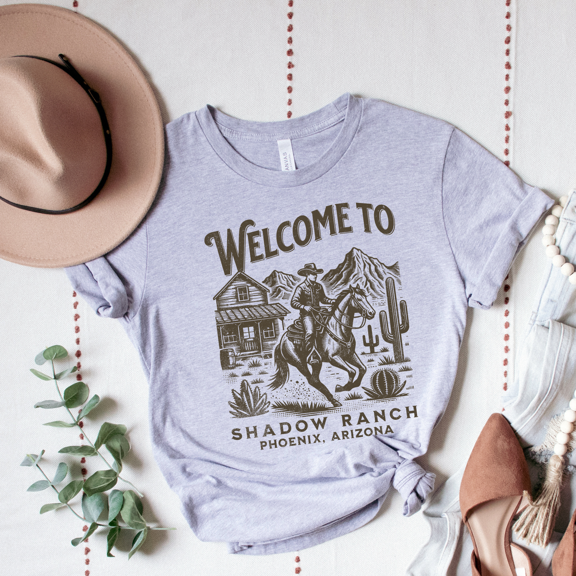 grey shirt that says "Welcome to Shadow Ranch Phoenix, Arizona" with a retro graphic of a cowboy riding on a horse.