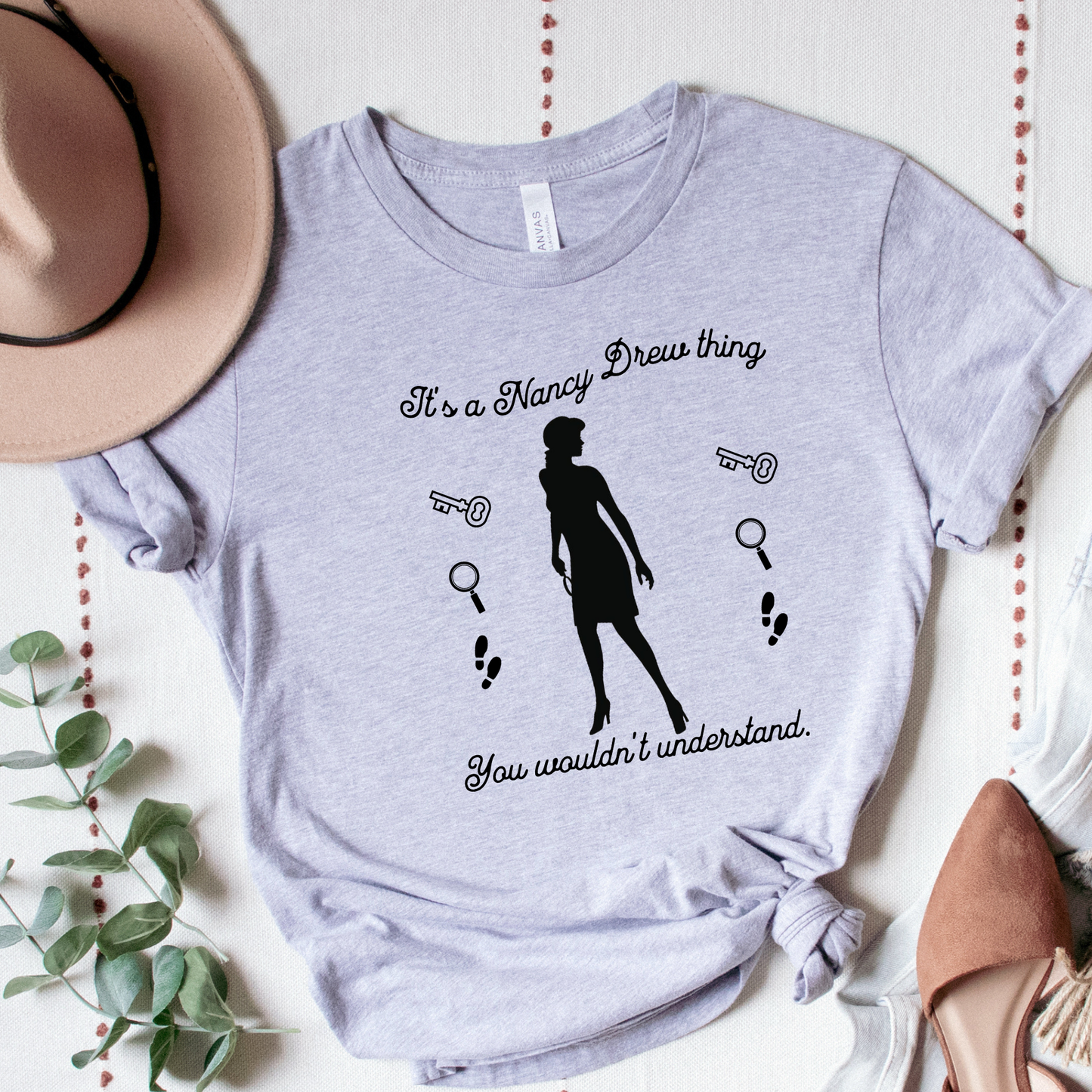 grey tshirt with text that says "It's a Nancy Drew thing, you wouldn't understand" with graphic elements like a key, magnifying glass and footsteps.