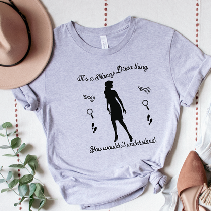 grey tshirt with text that says "It's a Nancy Drew thing, you wouldn't understand" with graphic elements like a key, magnifying glass and footsteps.
