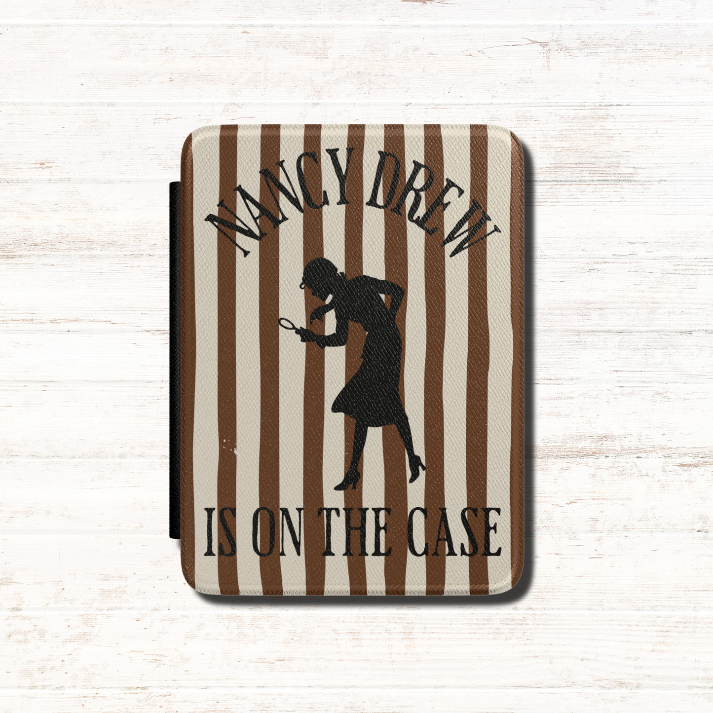 A Nancy Drew Kindle Case that features brown stripes, with a black silhouette of Nancy Drew with a magnifying glass and the text 'NANCY DREW IS ON THE CASE'. Designed by Starlit Prose Bookish Merch Australia.