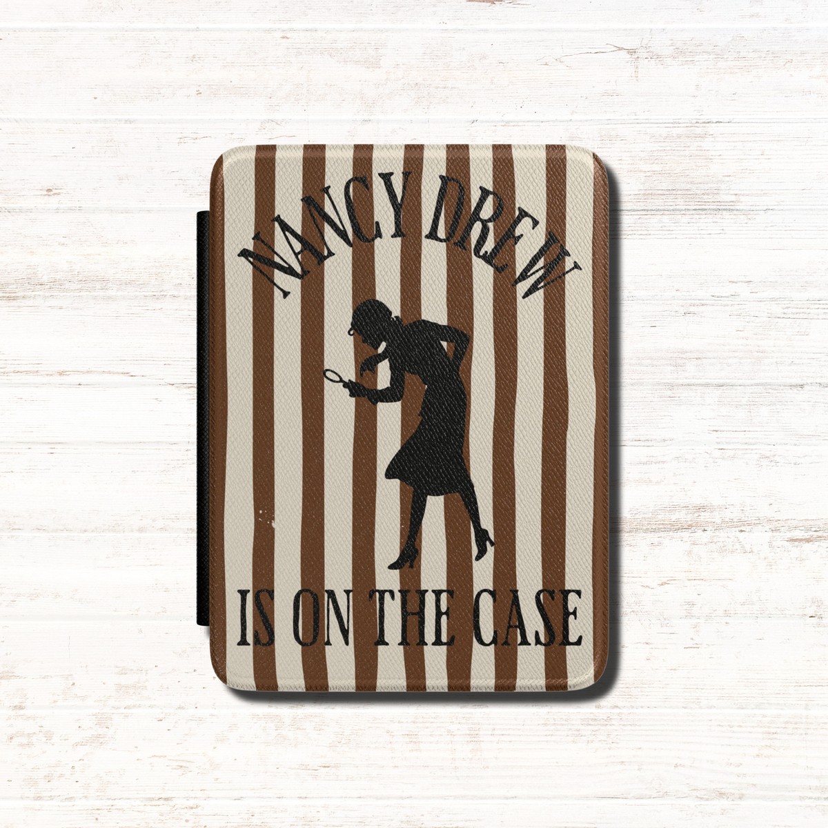 A Nancy Drew Kindle Case that features brown stripes, with a black silhouette of Nancy Drew with a magnifying glass and the text 'NANCY DREW IS ON THE CASE'. Designed by Starlit Prose Bookish Merch Australia.