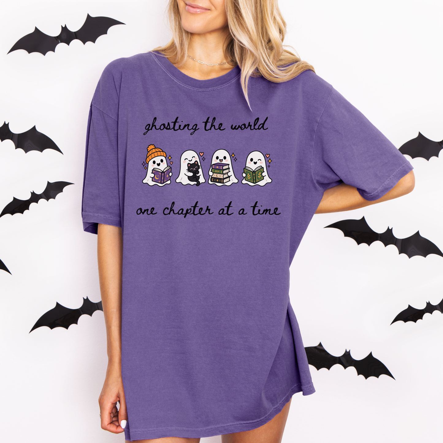 A woman wearing an oversized Grape Comfort Colors T-shirt with four cartoon ghosts reading books and the text 'ghosting the world one chapter at a time". Designed by Starlit Prose Bookish Merch Australia