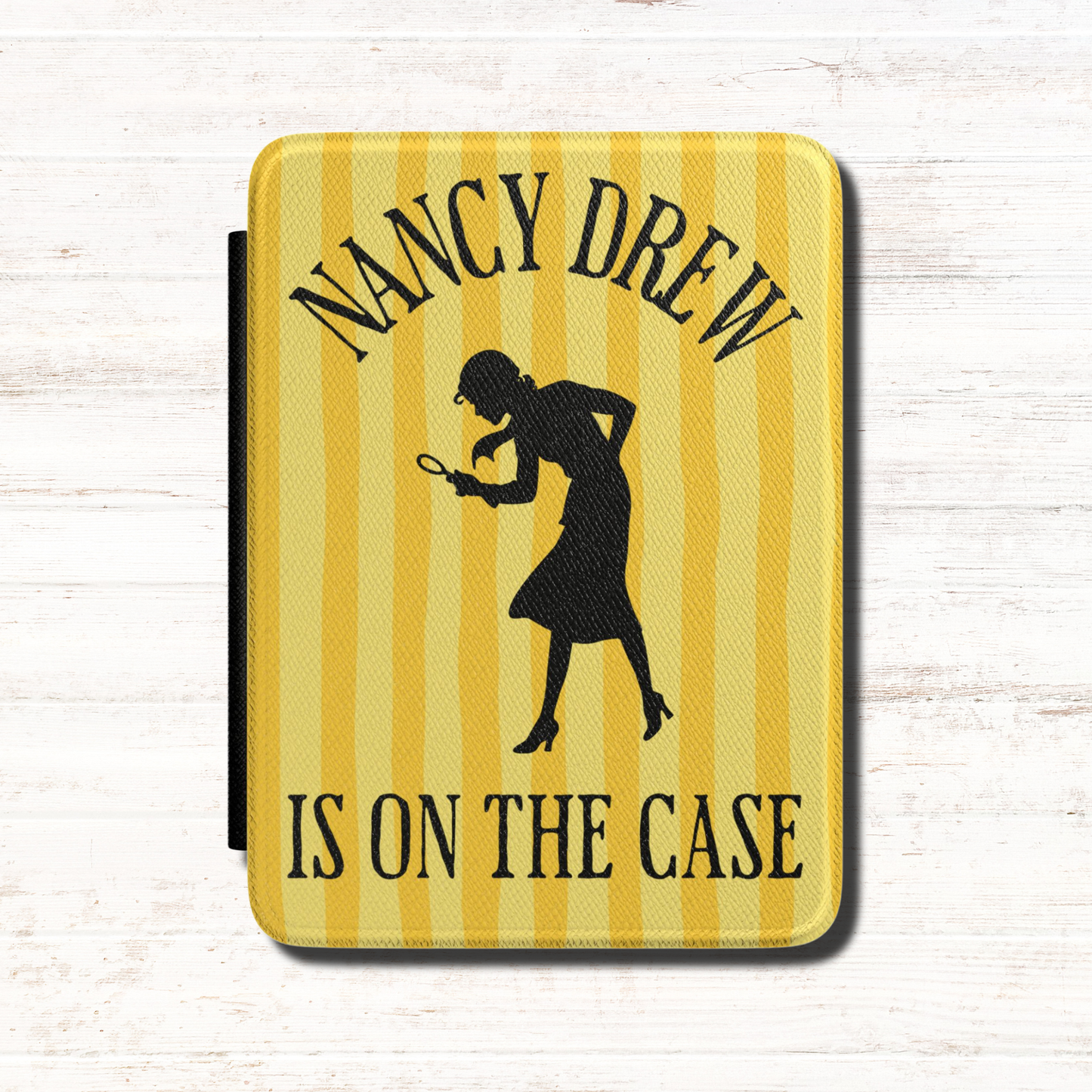A Nancy Drew Kindle Case that features yellow stripes, with a black silhouette of Nancy Drew with a magnifying glass and the text 'NANCY DREW IS ON THE CASE'. Designed by Starlit Prose Bookish Merch Australia.