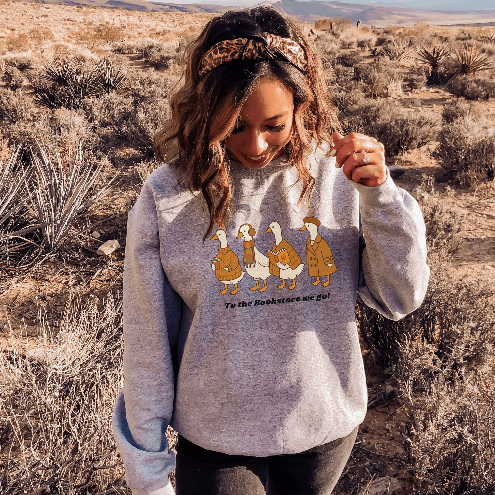 Woman wearing a grey sweatshirt with ducks going to a bookstore graphic. Starlit Prose Bookish Merch Australia