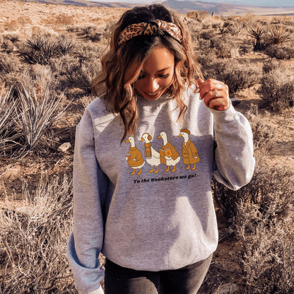 Woman wearing a grey sweatshirt with ducks going to a bookstore graphic. Starlit Prose Bookish Merch Australia