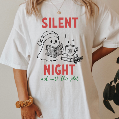 A woman wearing a white Comfort Colors t-shirt with a cute doodle illustration of a ghost reading a book, with a cup of coffee stacked on some books. There's bold text that says  'SILENT NIGHT" in red, with green cursive that says " not with this plot". Designed by Starlit Prose Bookish Merch Australia.