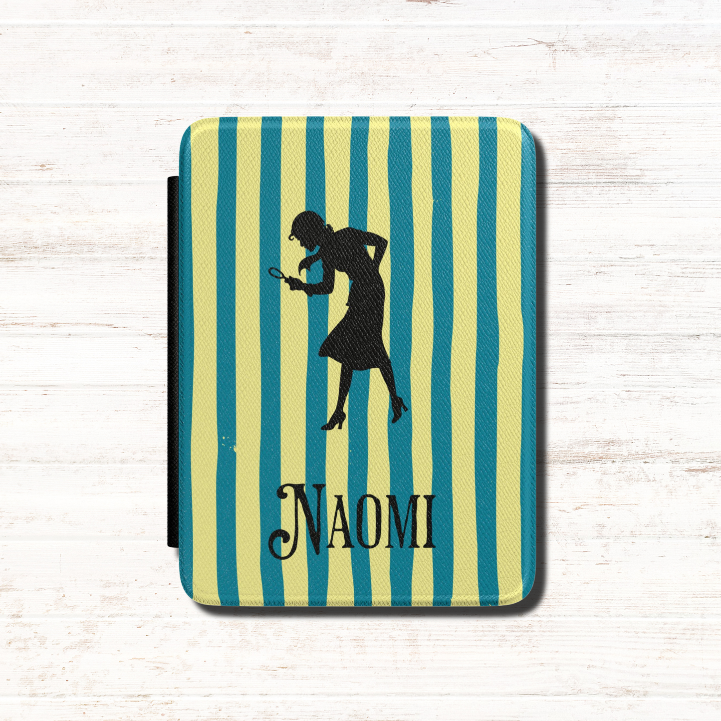 A close-up of a Personalised Nancy Drew Kindle Case, featuring a blue and yellow vertical stripe pattern with a black silhouette of Nancy Drew holding a magnifying glass and a custom name in vintage style typography at the bottom. Designed by Starlit Prose Bookish Merch Australia.